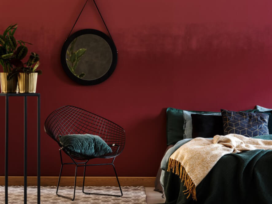 Bold red bedroom with deep green chair and bedding with cosy cream rug and plant with mirror